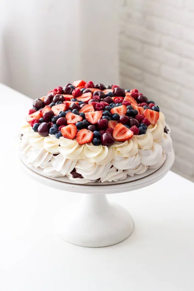 Baiser-Kuchen mit Schlagsahne und frischen Beeren, Erdbeeren, Blaubeeren, Himbeeren und Kirschen auf weißem Tisch. Stockbild