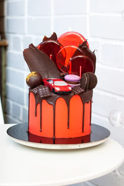 Red cake with chocolate racing car, chocolate decoration, macaroons, lollipops and cookies. White background.