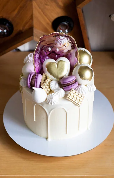 Modern elegant cake with melted white chocolate, golden heart and chocolate balls, macaroons, meringue and caramel.