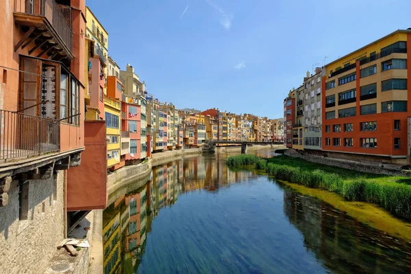 Kleurrijke gele en oranje huizen en Eiffel Bridge, oude vis kraampjes, weerspiegeld in water rivier Onyar, in Girona, Catalonië, Spanje. Kerk van Sant Feliu op achtergrond. — Stockfoto