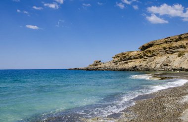 Berrak mavi suları, küçük çakıl taşları ve kumları olan tenha bir sahil.,