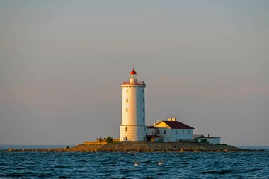 Gün batımında körfezin ortasındaki taş adadaki fener.