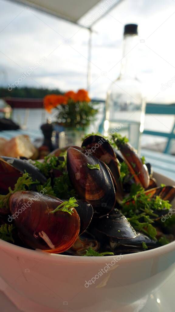 Bowl of mussels with cream, onion and parsley served with a bottle of white wine on the terrace during a summer evening
