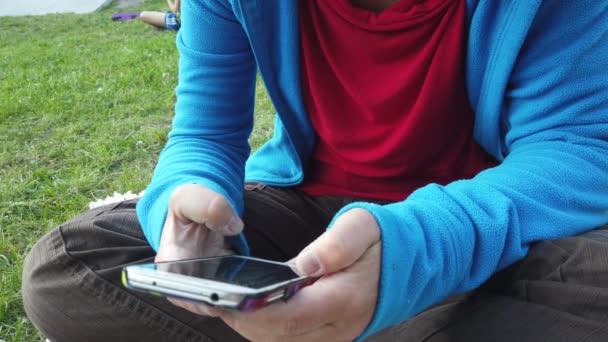 一个年轻女人坐在草坪上看着手机时的双手 — 图库视频影像