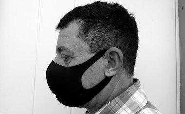 Siyah koruyucu anti-salgın maskeli bir adamın yüzünü tasvir eden siyah ve beyaz bir görüntü.