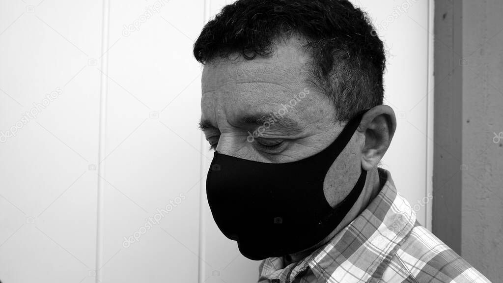 Black and white image that portrays the face of a man with a black protective anti-contagion mask