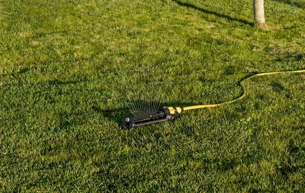 ポータブルで効率的な金属アーム付き振動スプリンクラーは 公共の通りの芝生エリアに水のファンを吹き出します 夏に調整可能な振動スプリンクラーによって都市の芝生に水をやる — ストック写真