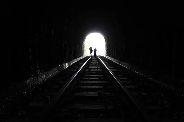 Silhouettes of people walking along the tracks of old railway tunnel built in rock wall