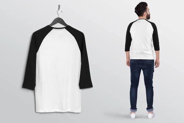 Hanging white and black blank raglan shirt on wall with standing male model. Back view. Isolated background.