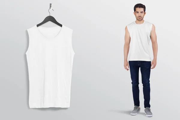 Hanging white plain sleeveless shirt on wall, with male model in dark blue denim jeans pant. Isolated background.