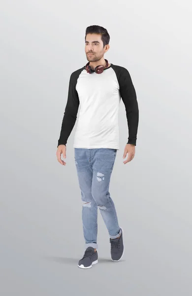 ブルーのフリップデニムジーンズパンツに白と黒の無地のラグランロングスリーブシャツを着た男性モデルを歩く 首の周りのヘッドフォン 隔離された背景 — ストック写真