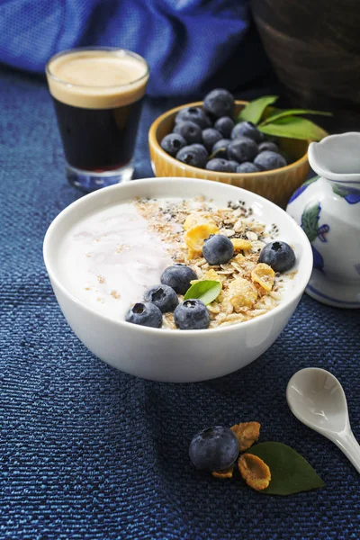 Healthy classic breakfast with yogurt, coffee and various cereals fresh blueberries on dark blue napkin. Text space.