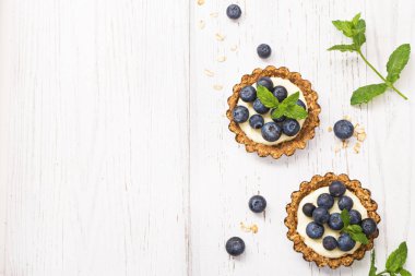 Krem ve yaban mersini ve serbest metin alanı olan beyaz tahta masada nane ile mini yulaf gevreği tart