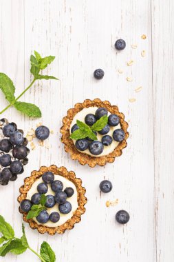 Krem ve yaban mersini ve serbest metin alanı olan beyaz tahta masada nane ile mini yulaf gevreği tart