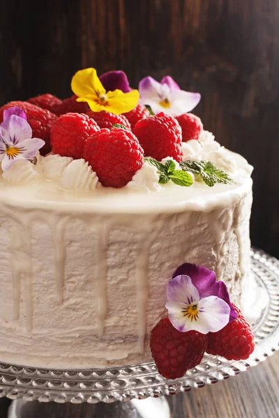 Festive cake with raspberries and flowers with streaks of glaze on  black background