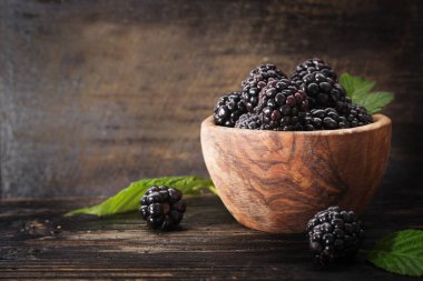 Böğürtlen serbest metin alanı ile eski karanlık tabloda ahşap kase. Tarım, bahçecilik, hasat kavramı. Seçici odak.