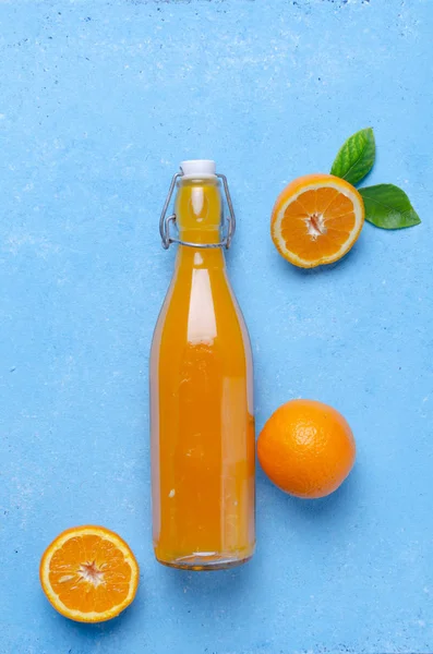 Orange juice in glass bottle with fruits on bright blue background
