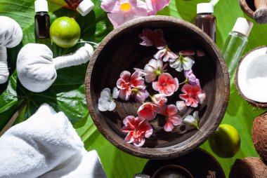 Tropikal çiçekli ahşap kase ve muz yapraklarında güzellik tedavisi için spa ürünleri..