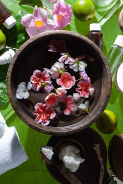 Tropikal çiçekli ahşap kase ve muz yapraklarında güzellik tedavisi için spa ürünleri..