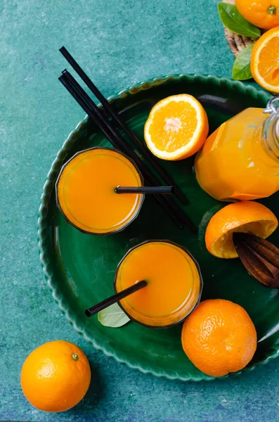 Fresh homemade orange juice in glass  in green ceramic plate, over turquoise table. Rustic stile.