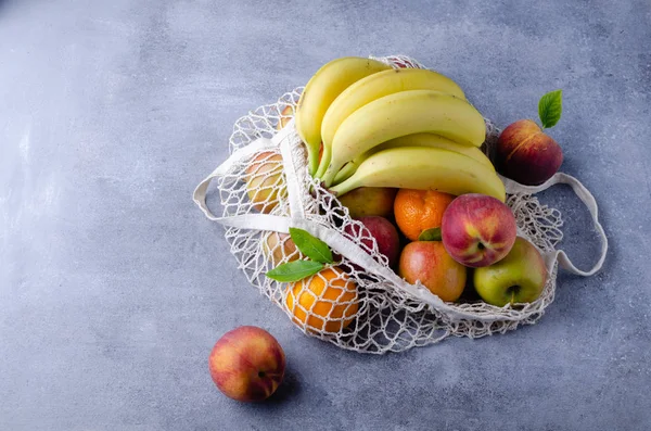 Fresh organic fruits in canvas cotton shopping eco friendly bag with  over grey blue table. Zero waste, plastic free concept.