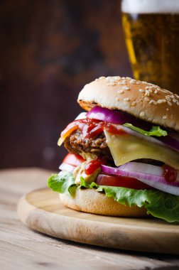 Pirpirit ile Geleneksel burger, taze sebze, ahşap bir masada cam bira ile susam ile gevrek topuz.