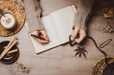 Sonbahar kış arka plan. Kadın el bir kroki veya mektup yün iplik ve cappuccino fincan ahşap bir arka planda bir top ile eski Notebook üzerinde bir kalem tutarak. Ev hobileri, Cozy konfor konsepti.