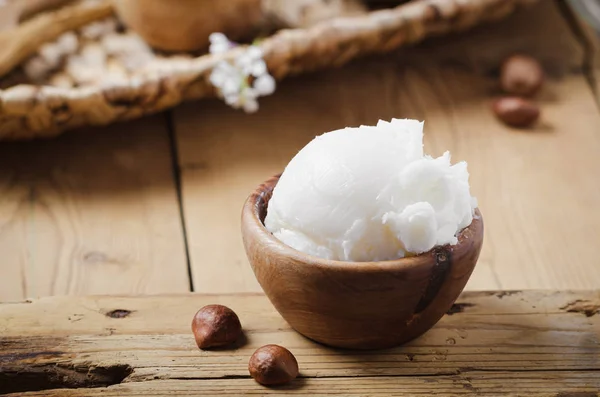 Shea butter in wooden bowl with nuts on old rustic table. — Stock Photo, Image