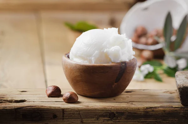 Shea butter in wooden bowl with nuts on old rustic table. — Stock Photo, Image