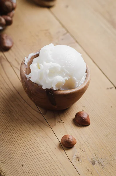 Shea butter in wooden bowl with nuts on old rustic table. — Stock Photo, Image
