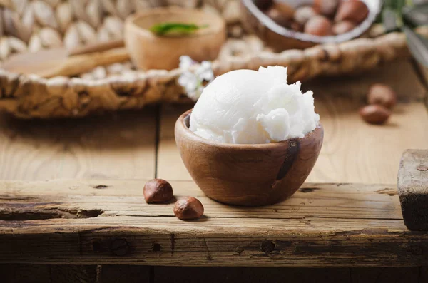 Shea butter in wooden bowl with nuts on old rustic table. — Stock Photo, Image