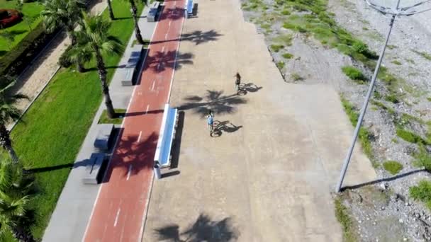 Vuelo aéreo detrás del niño y la niña montando bicicletas a lo largo de la playa — Vídeos de Stock