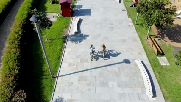 Воздушный полет за молодым парнем и девушкой на велосипеде по современной площади — стоковое видео