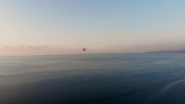 Aerial tracking of hang-glider that flying over the sea towards the setting sun — Stock Video