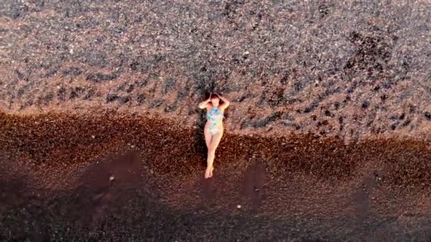 Вид с воздуха на молодую девушку, отдыхающую на пляже. Снято дроном на закате — стоковое видео