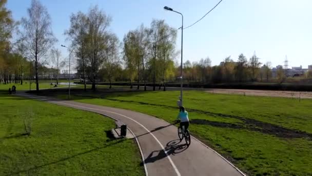 Воздушный полет для девушки, которая катается на велосипеде в парке. Снято беспилотником — стоковое видео