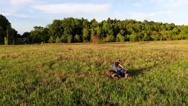 O tiroteio aéreo de um tipo está montado num ATV no campo verde. Tomado por drone — Vídeo de Stock