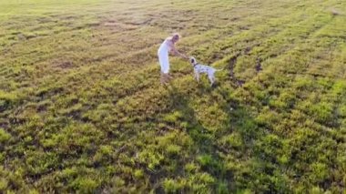 Beyaz elbiseli bir kız Dalmaçyalı köpeğiyle oynar ve onu eğitir. İnsansız hava aracı tarafından çekiliyor.