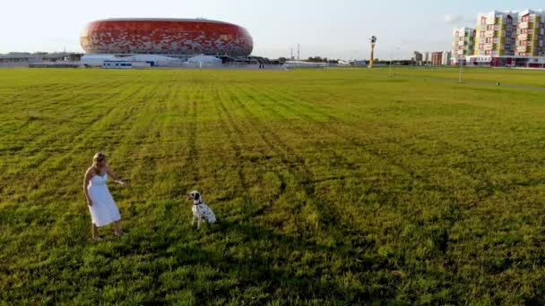 Menina em um vestido branco joga e treina seu cão dálmata. Tomado por drone — Vídeo de Stock