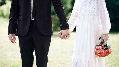 Yaz parkında el ele tutuşan aşıklar, yaz parkında el ele tutuşuyor. Güzel klasik tarzı ile Weddind gün. Gül buketi ile beyaz elbiseli güzel gelin.
