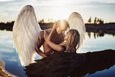 Romantic meeting of angels. Good and evil. A parken and a girl stand by the water at sunset. clipart