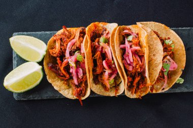 Siyah arka planda Meksika tacoları. Cochinita pibil (doğranmış et, soğan ve baharatla), kişniş ve limon ile doldurulmuş.