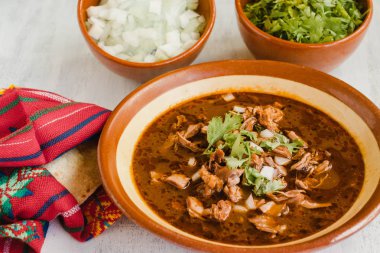 Birria de res beyaz bir masada, onu hazırlamak için gerekli tüm malzemelerle birlikte. Tipik Meksika tarifi.