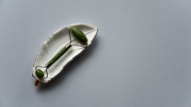 Yüz masajı için Jade Roller ya da seramik tabakta gua sha. Mavi kağıt arka plan. Üst Manzara. Boşluğu kopyala.