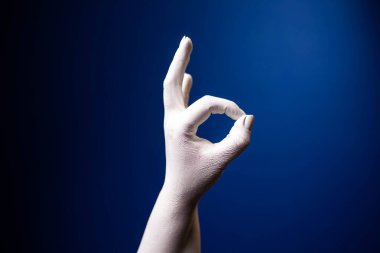 El hareketi. İnsan jesti. Mavi arka planda iki parmak tamam diyor. Mavi arka planda beyaz bir el.