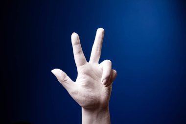 El hareketi. İnsan jesti. Mavi arka planda iki parmak selam veriyor. Mavi arka planda beyaz bir el.