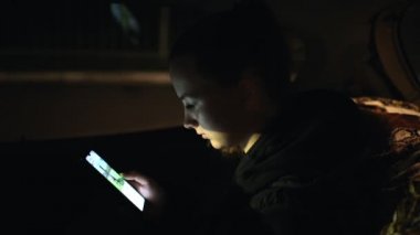 Genç bir kız gece bir arabada oturur ve telefona bakar. Akıllı telefonuyla karanlıkta oturan bir kız.