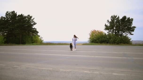 Девушка со взрослым псом переходит дорогу и направляется к камере — стоковое видео