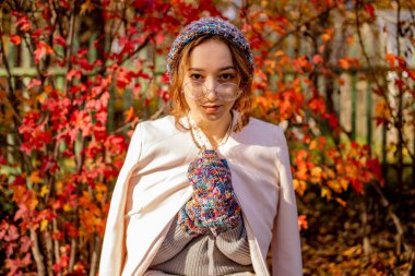 Kırmızı sonbahar yapraklarının arka planında duran güzel ince kız. Sonbaharda sıcacık giyimli kadın.