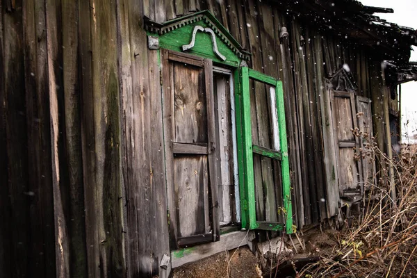 broken windows of an old wooden house in snowfall. Windows of a country house with broken glass